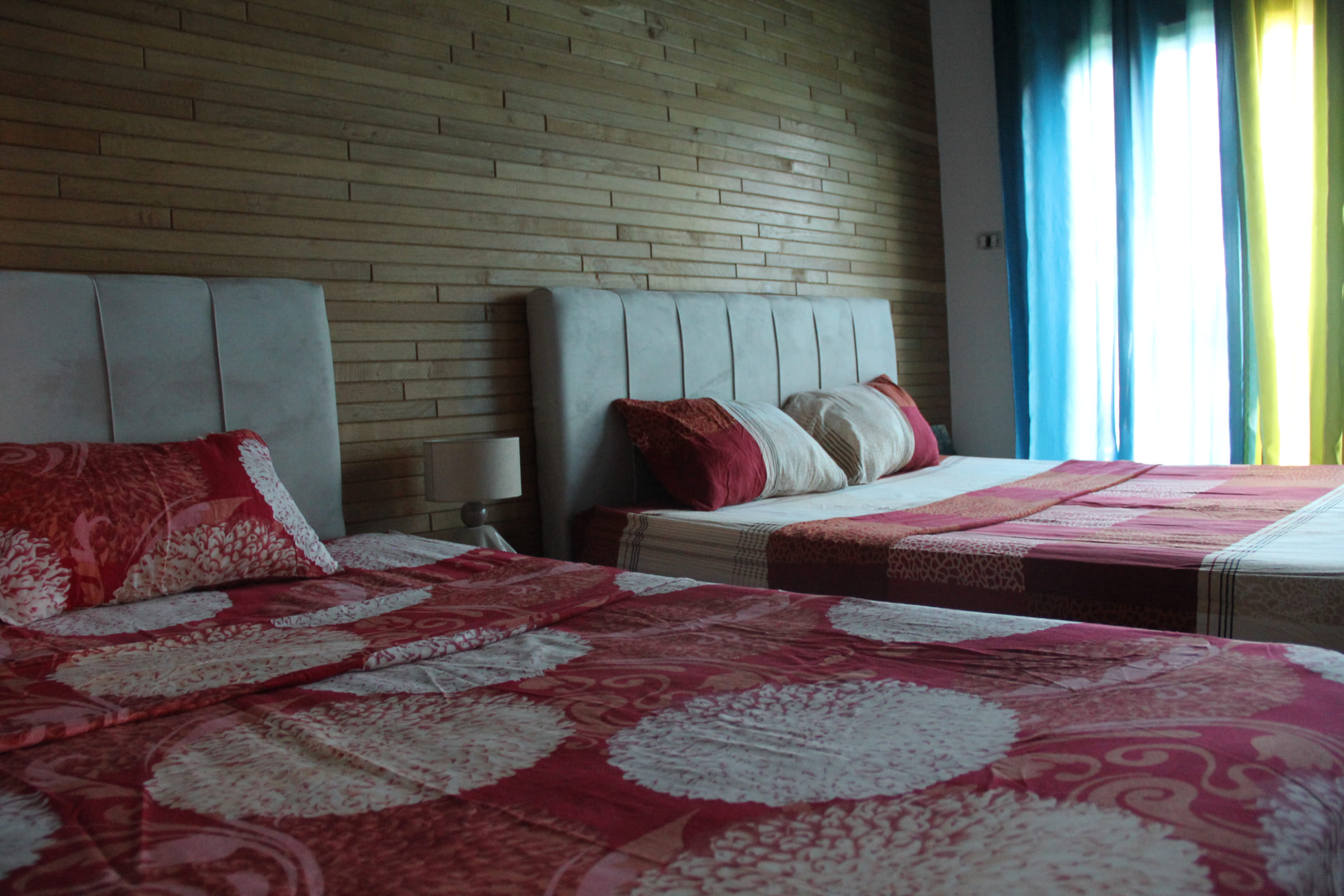 Chambre quadruple avec deux grands lits et couvre-lits rouges, fenêtre sur la verdure